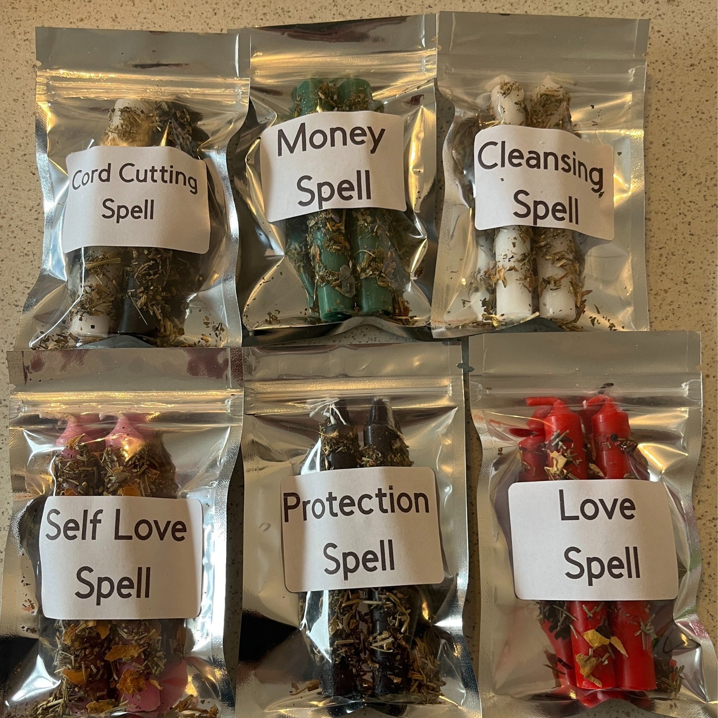 Six packages of herbs labeled with various spells on a textured surface.