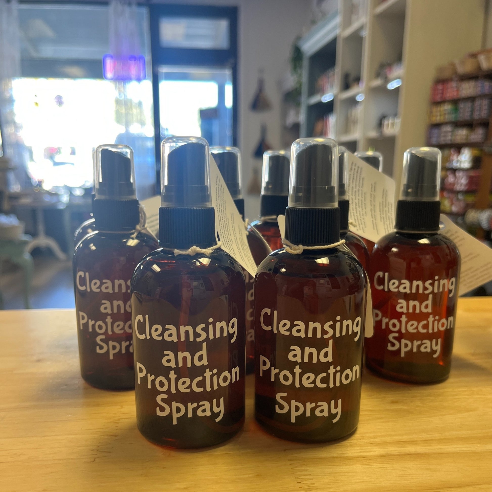 Bottles of 'Cleansing and Protection Spray' on a wooden surface with a store interior in the background.