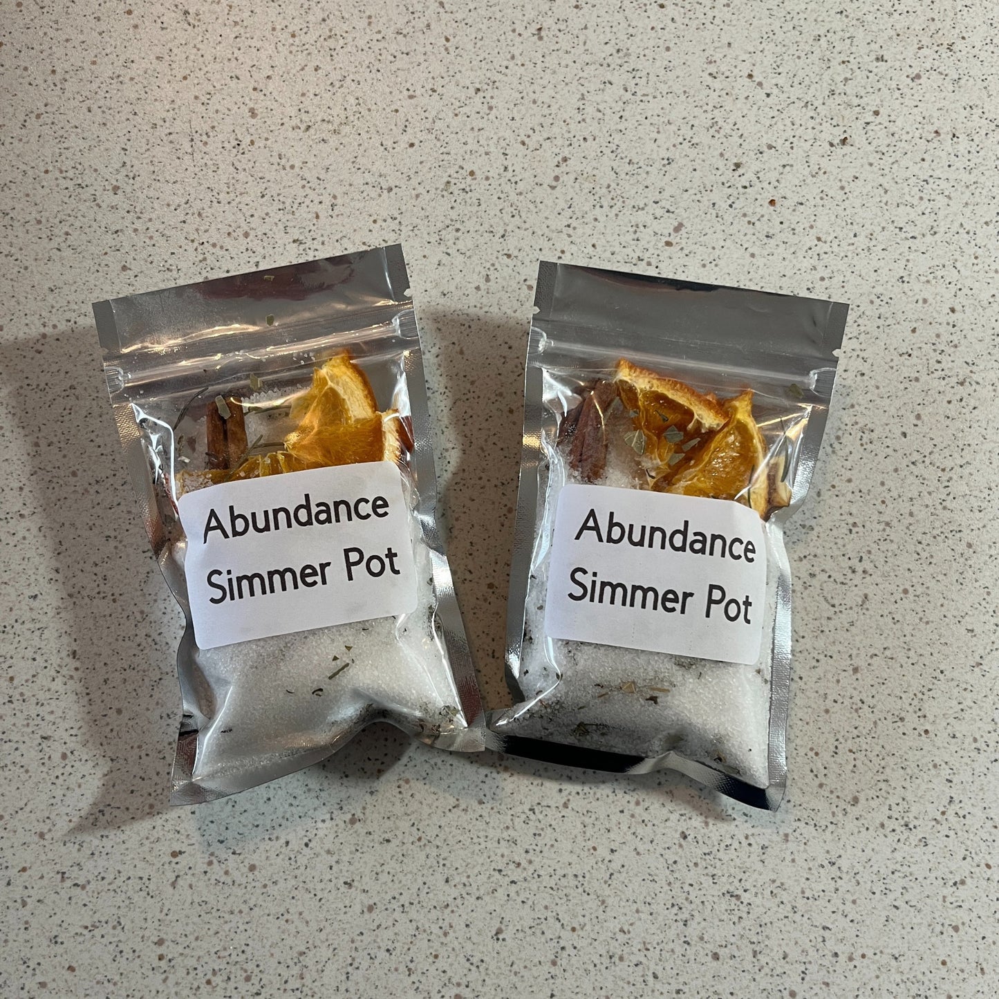 Two packages of 'Abundance Simmer Pot' on a speckled countertop