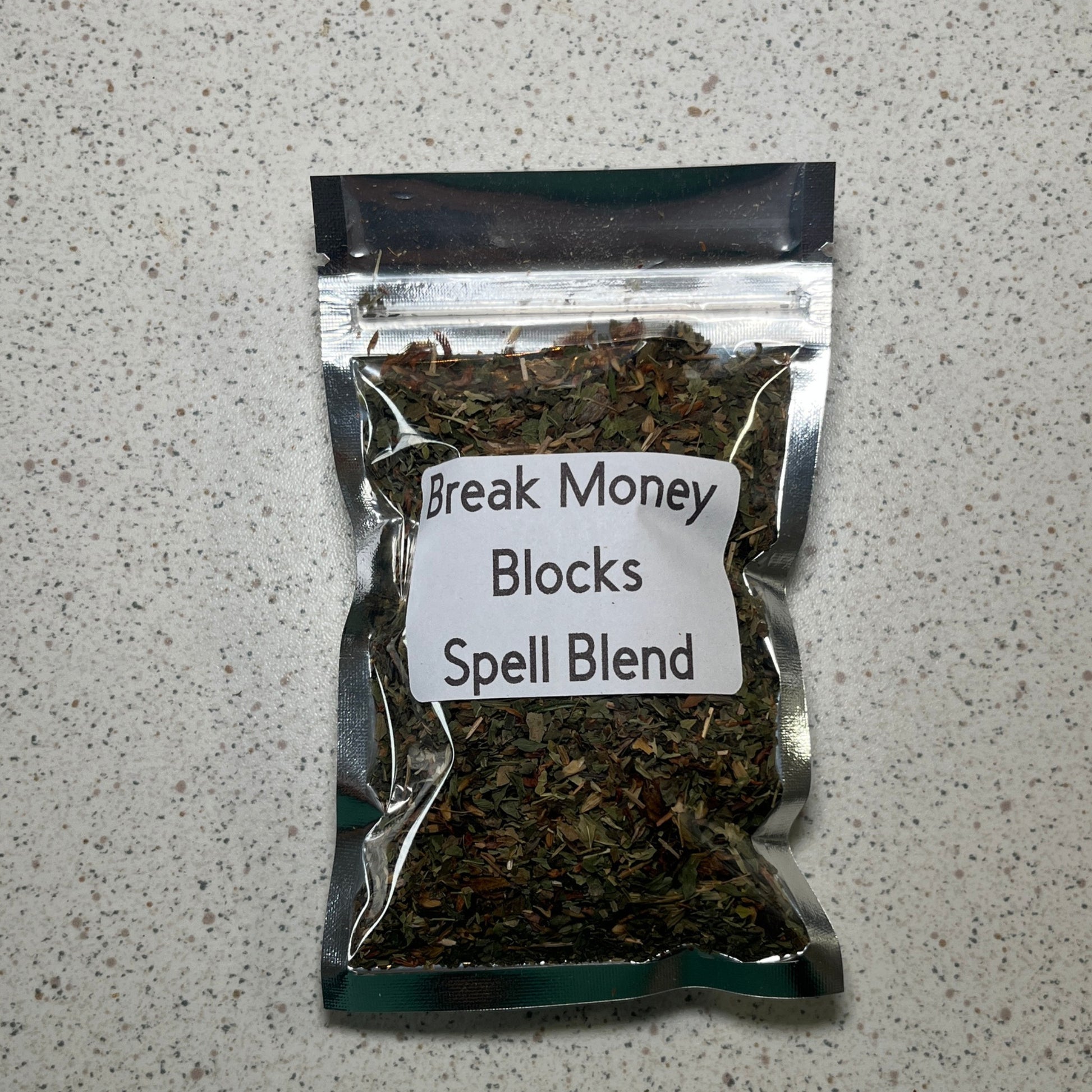 Packaged spell blend labeled 'Break Money Blocks' on a speckled gray surface