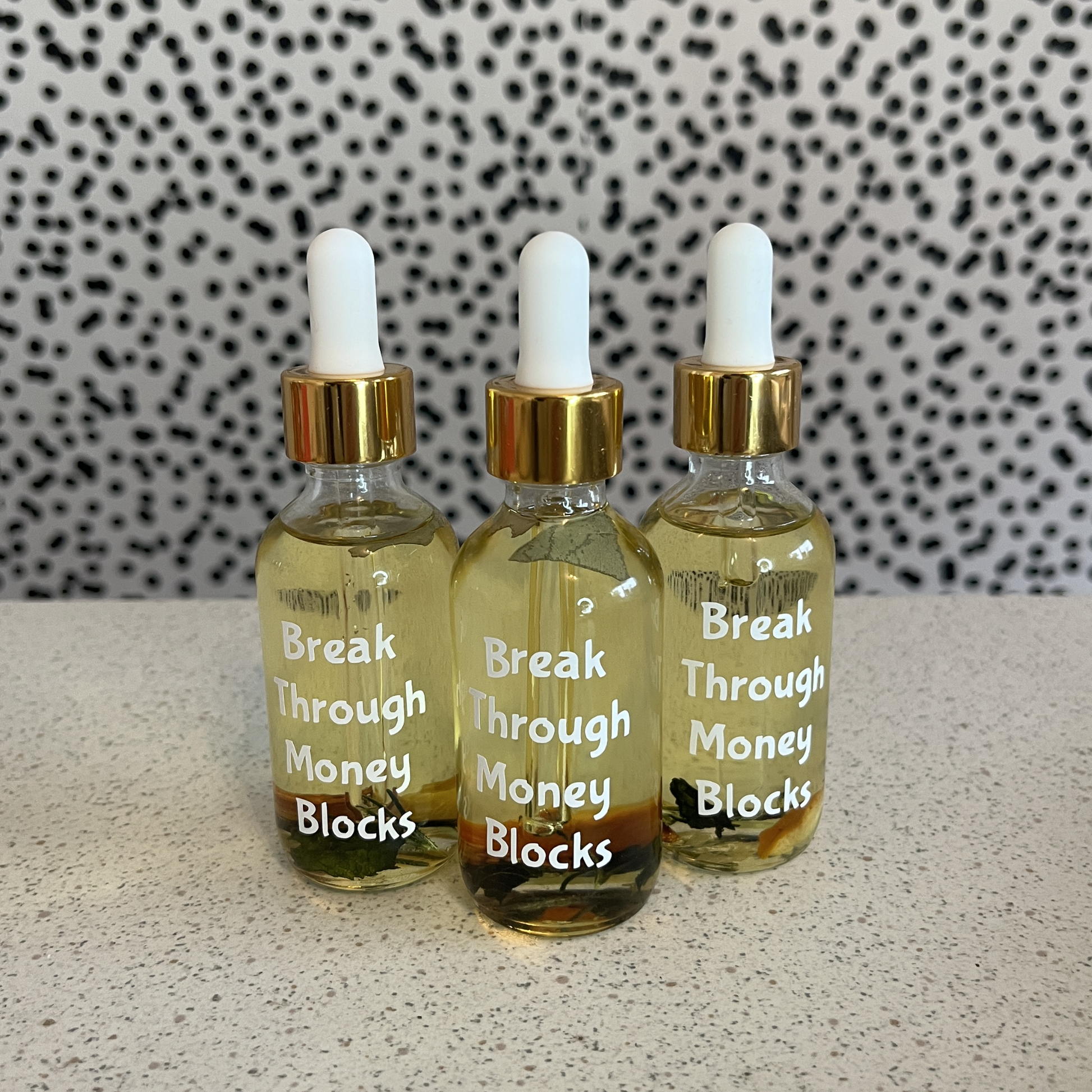 Three dropper bottles with gold caps and labels on a textured surface with a patterned background.