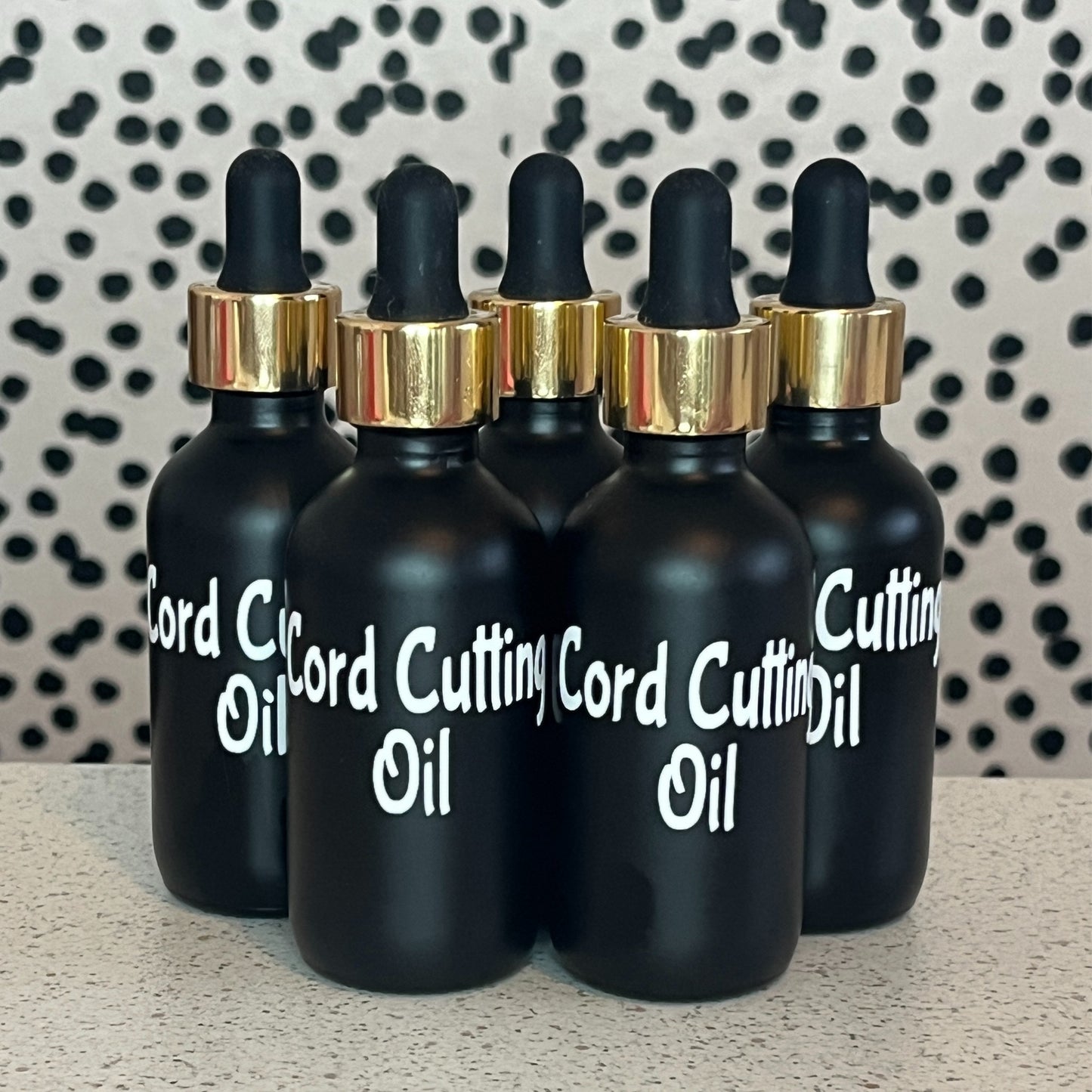 Four black dropper bottles labeled 'Cord Cutting Oil' on a patterned background
