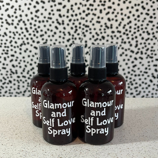 Set of 'Glamour and Self Love Spray' bottles on a speckled surface with a patterned background.