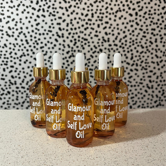 Five bottles of 'Glamour and Self Love Oil' on a textured surface with a patterned wall in the background.