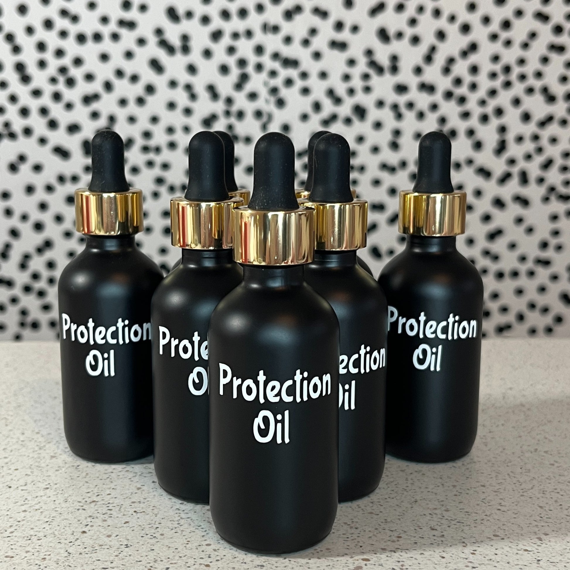 Black dropper bottles labeled 'Protection Oil' on a speckled surface with a patterned wall in the background.