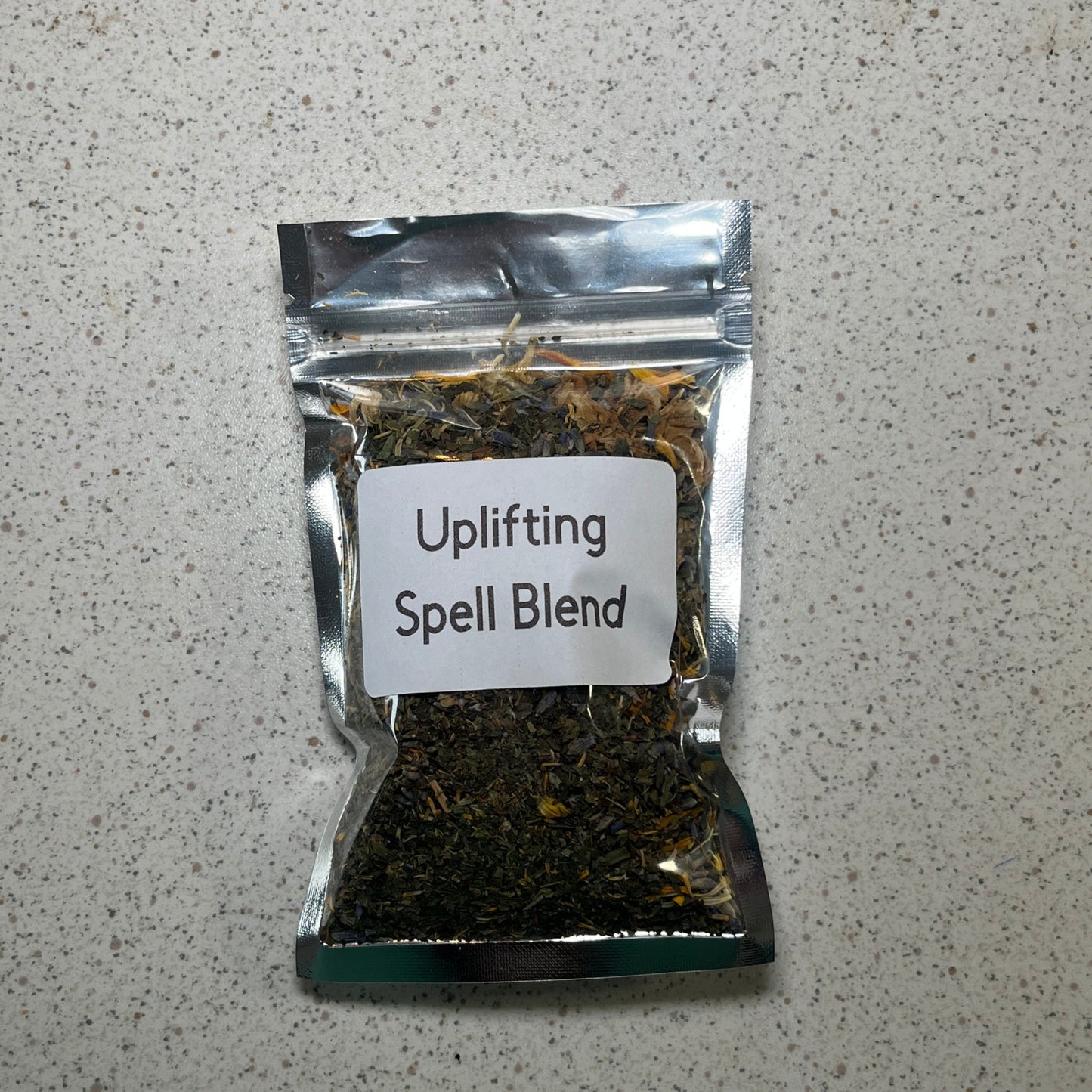 Packaged 'Uplifting Spell Blend' on a speckled gray surface