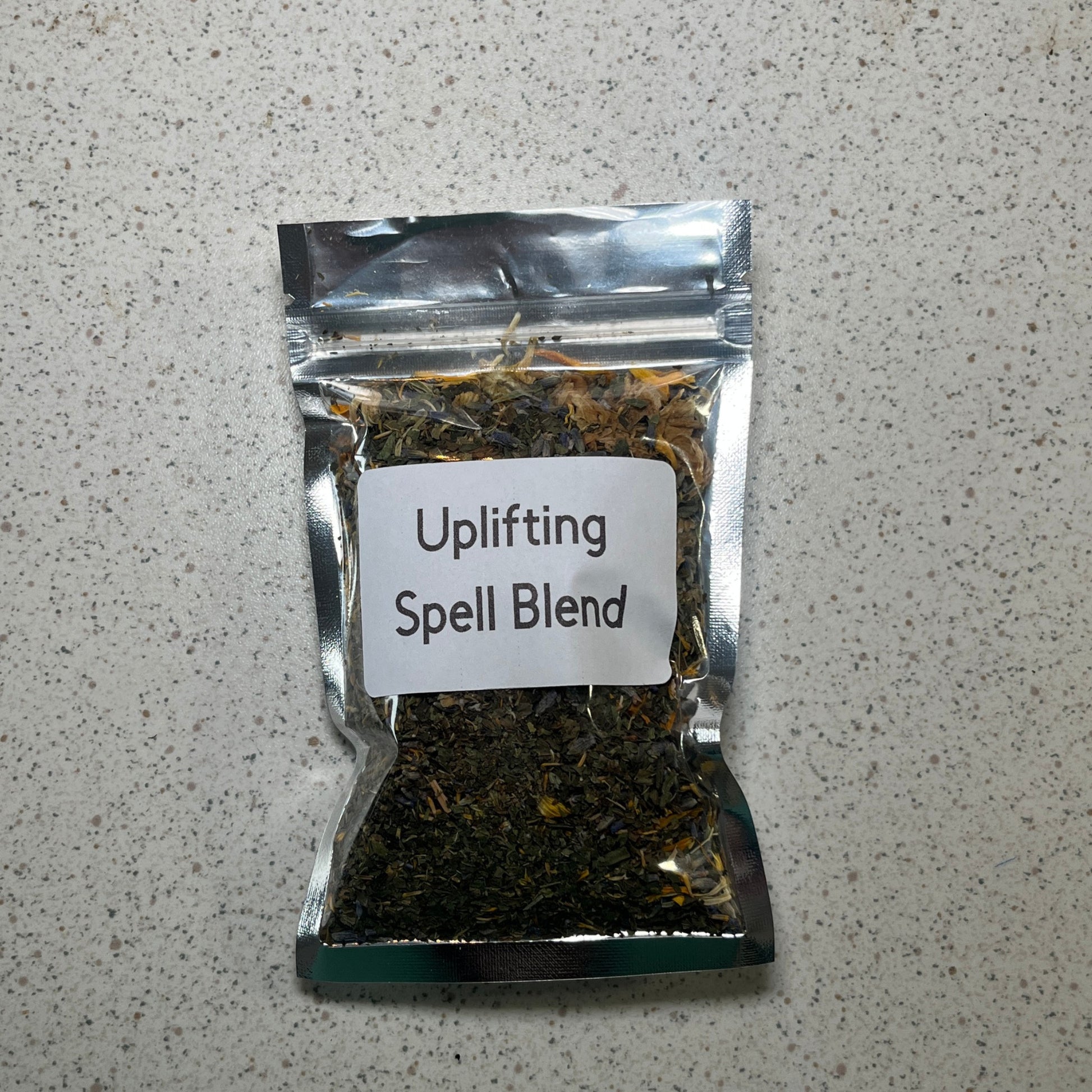 Packaged 'Uplifting Spell Blend' on a speckled gray surface